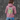 Person wearing a pink hoodie with a colorful design on the back against a dark textured wall.