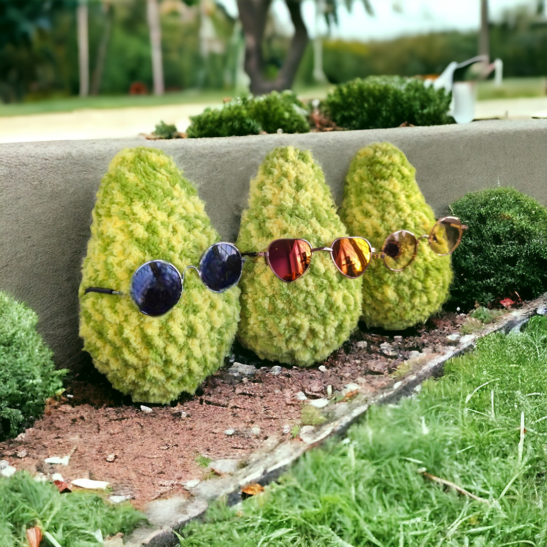 Three crochet cannabis leaf toys with sunglasses in a garden