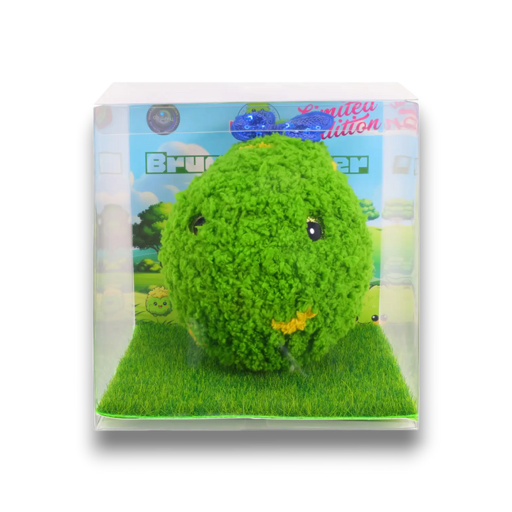 The original Bruce Hashie® plush, the first-ever Hashies® design, showcased in a collector’s edition display box. This limited-edition terpene-infused plush features a soft, fuzzy green texture, a charming embroidered smile, and a playful blue bow. The packaging includes a grass-textured base and a whimsical illustrated backdrop, emphasizing Bruce’s nature-inspired design. A must-have for Hashies® collectors and aromatherapy enthusiasts.